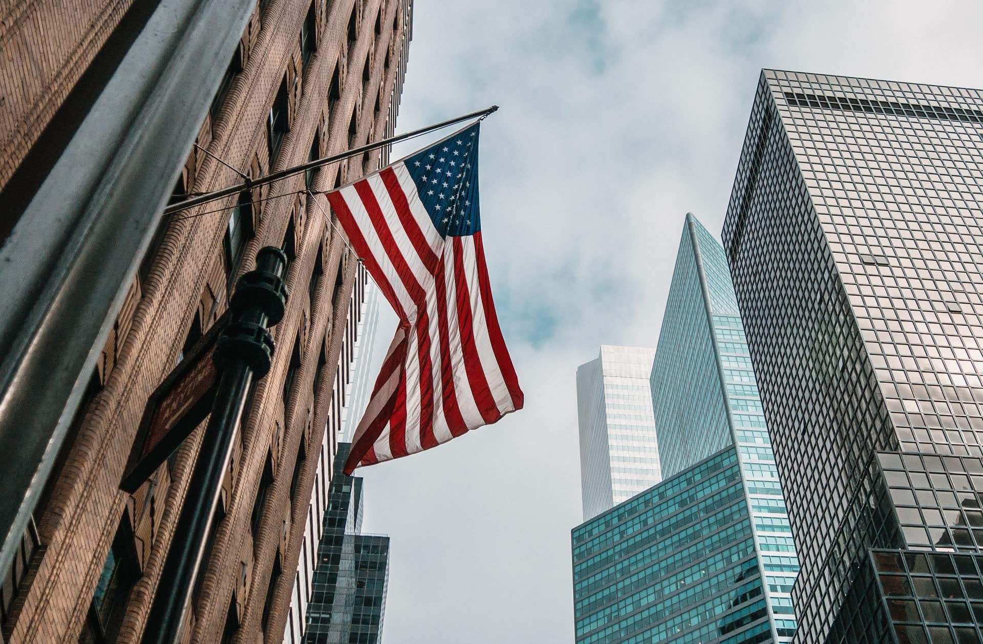 Drapeau américain devant les gratte-ciels d'un quartier d'affaires, aux États-Unis. Vivre aux États-Unis : notre fiche expatriation.