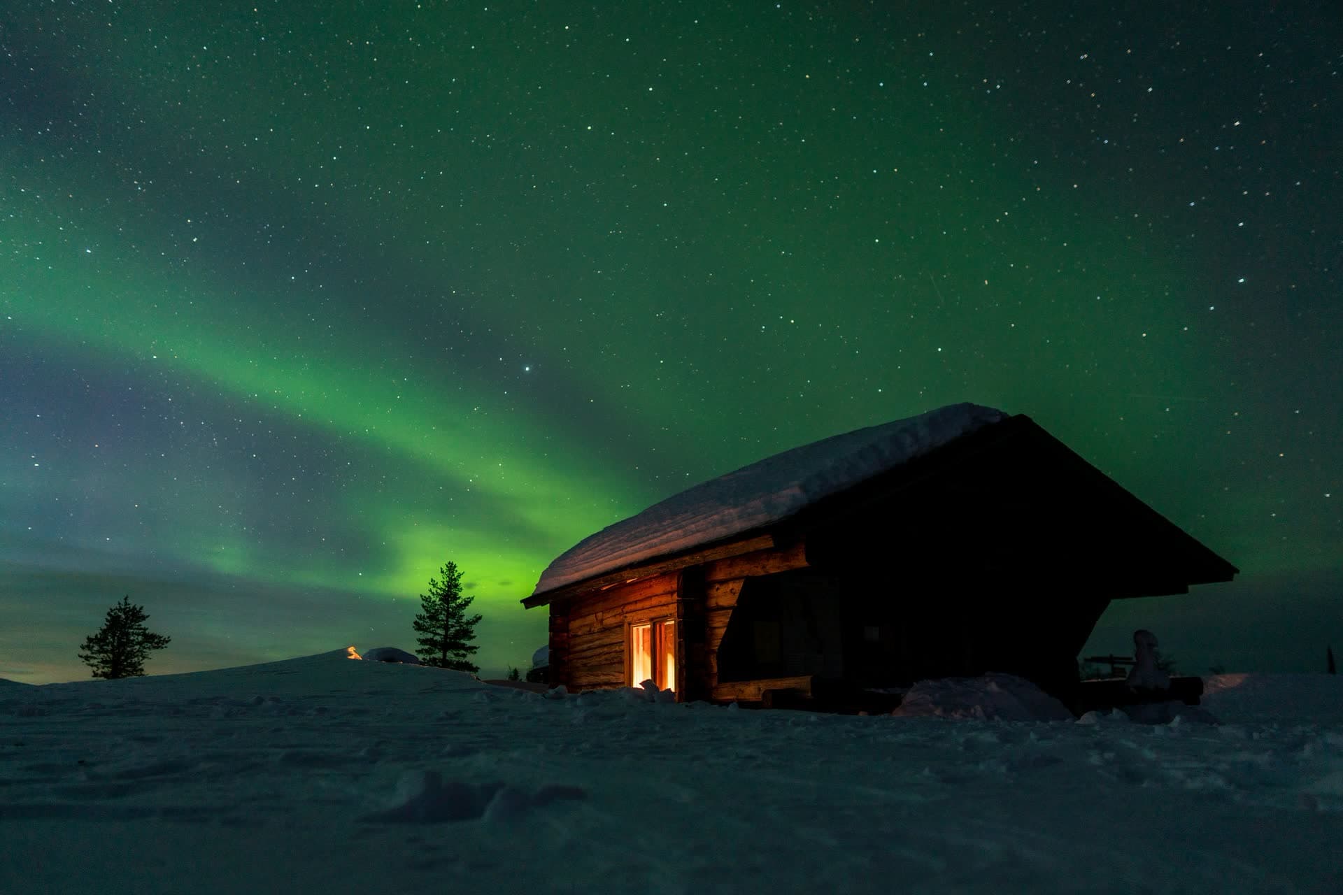 Aurore boréale au-dessus d'un chalet en bois, en Finlande. Vivre en Finlande : notre fiche expatriation.