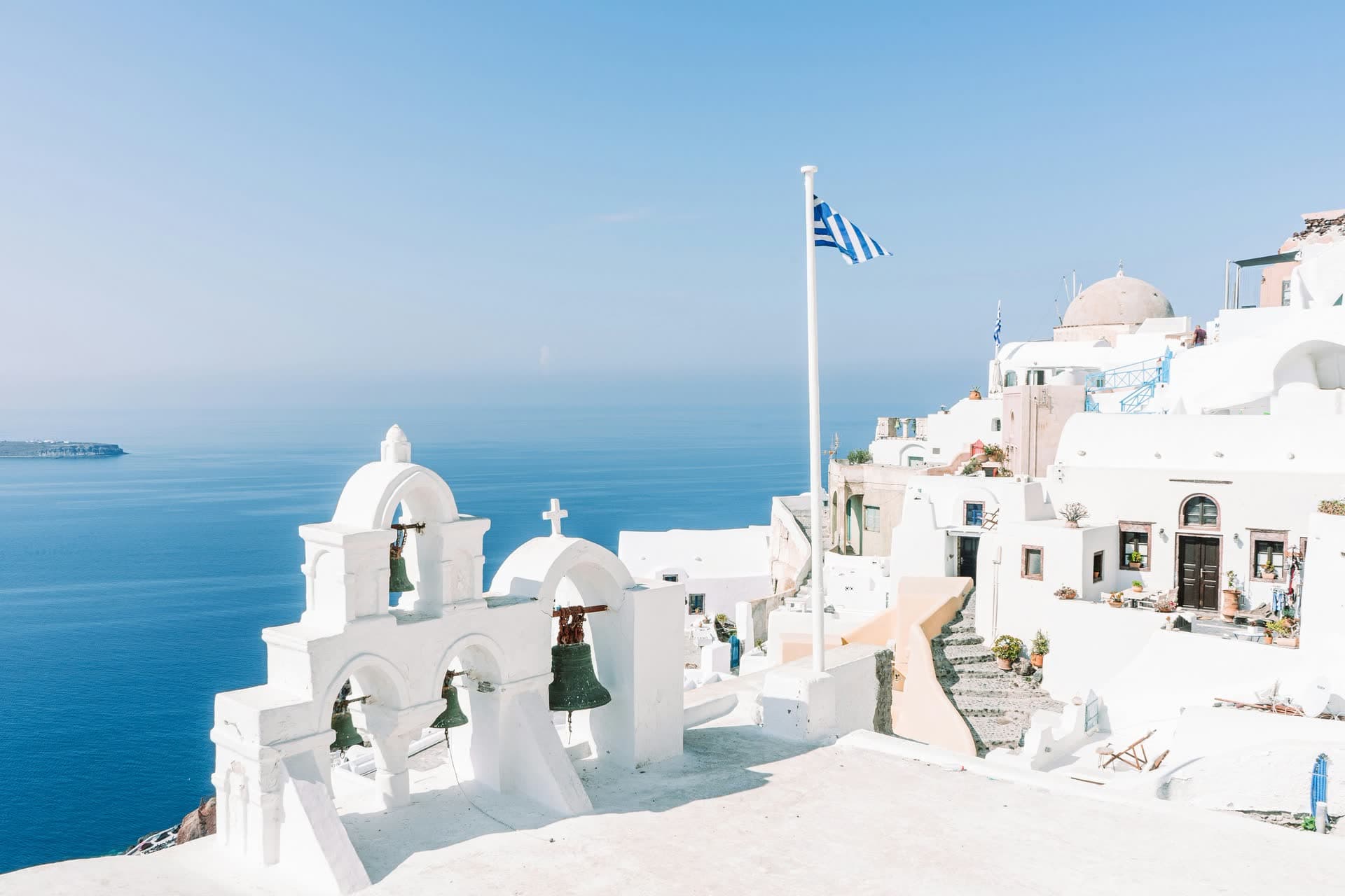 Église blanche à coupole bleue et cloches face à la mer Égée, en Grèce. Vivre en Grèce : notre fiche expatriation.