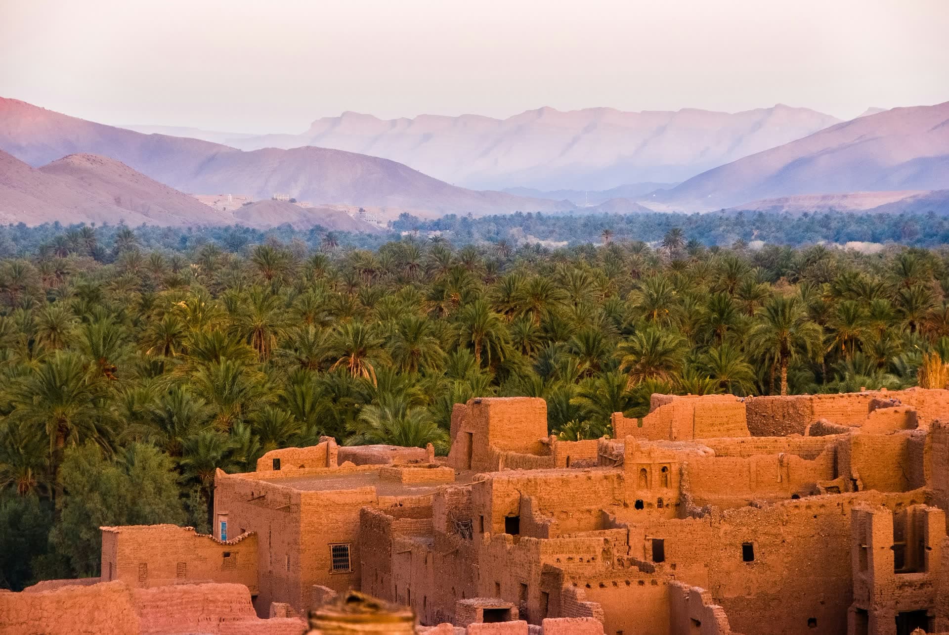 Ksar en pisé devant la palmeraie et les sommets de l'Atlas, au Maroc. Vivre au Maroc : notre fiche expatriation.