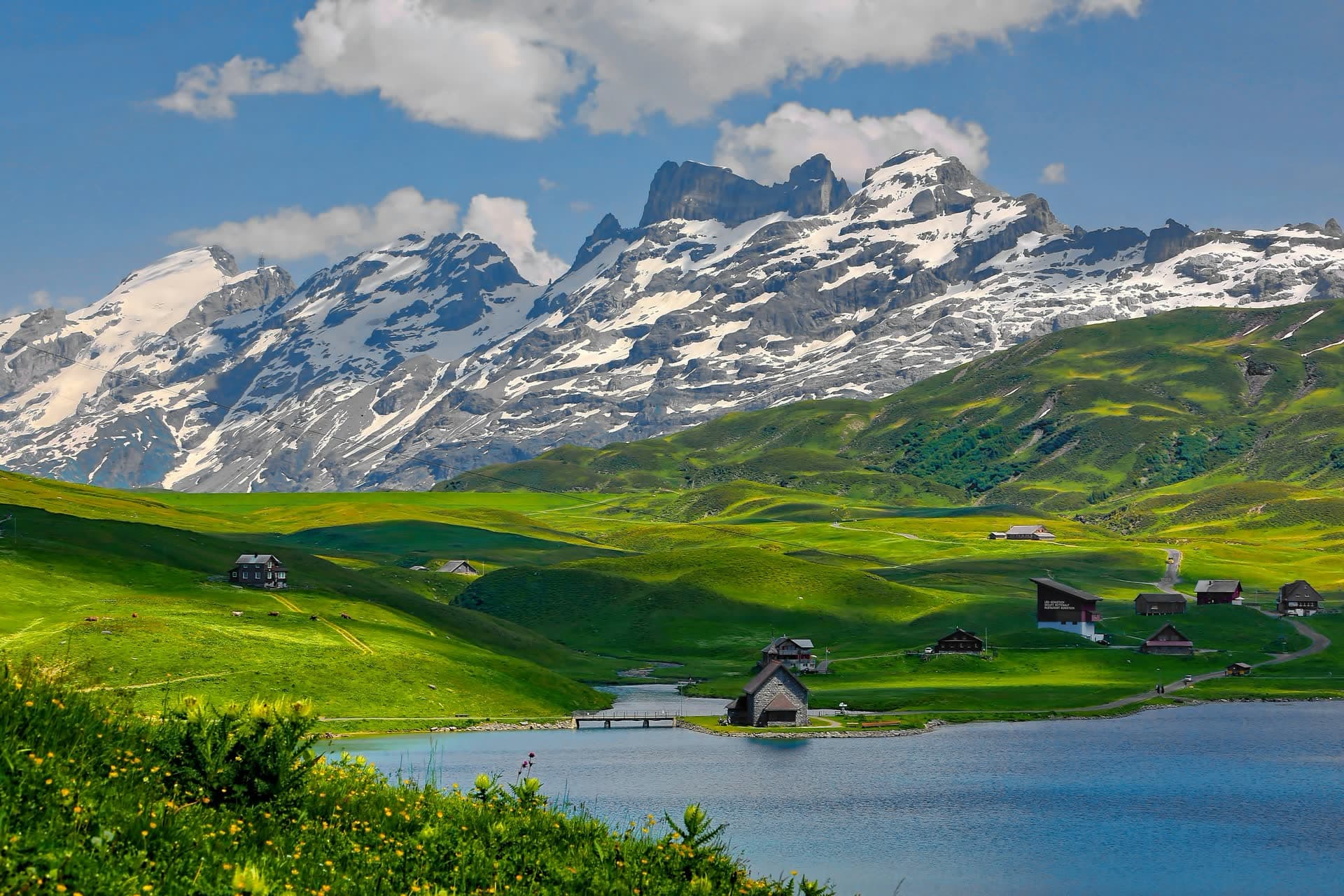 Alpage et lac devant les sommets enneigés, en Suisse. Vivre en Suisse : notre fiche expatriation.