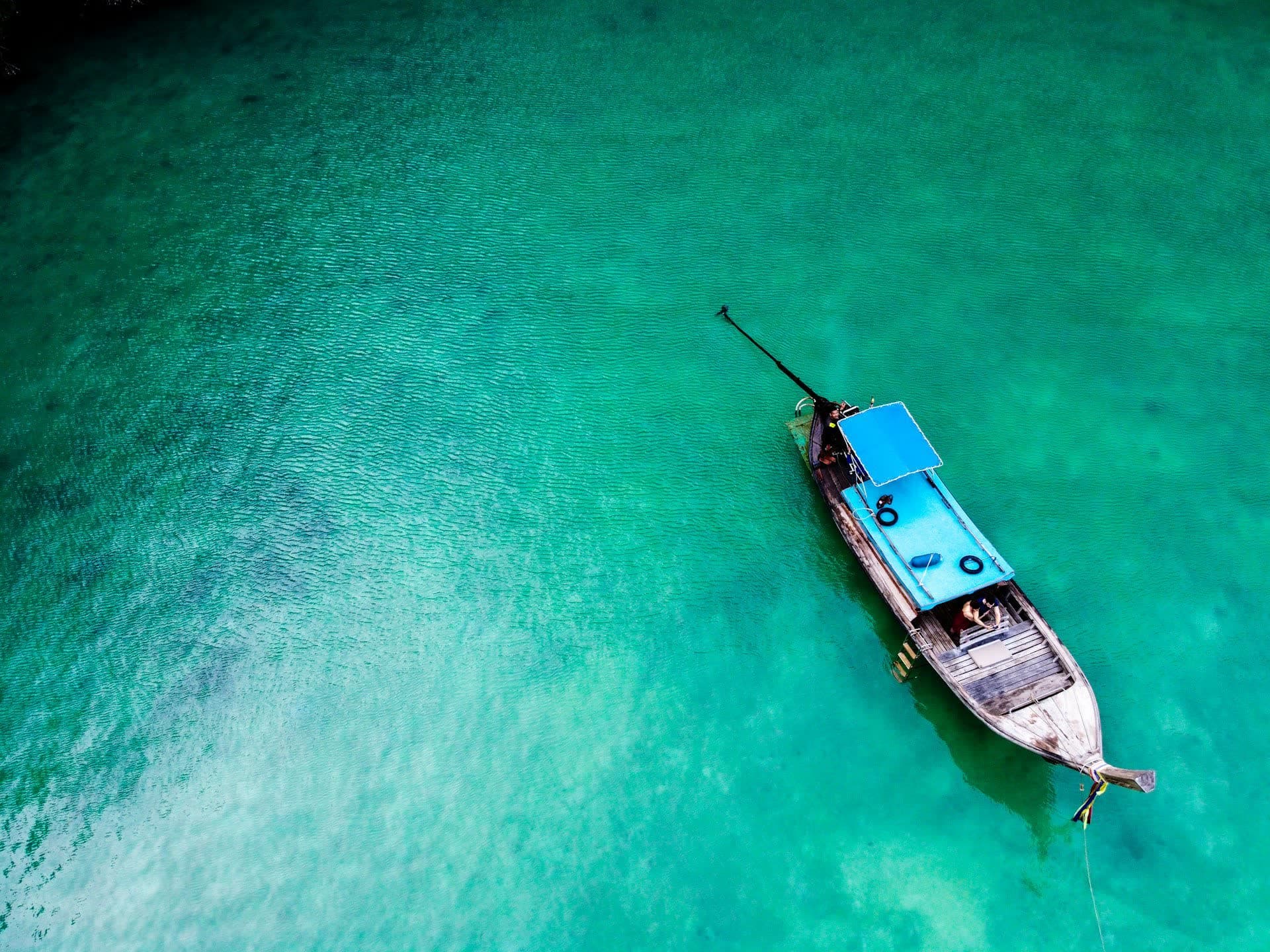 Bateau longtail sur une eau turquoise, en Thaïlande. Vivre en Thaïlande : notre fiche expatriation.